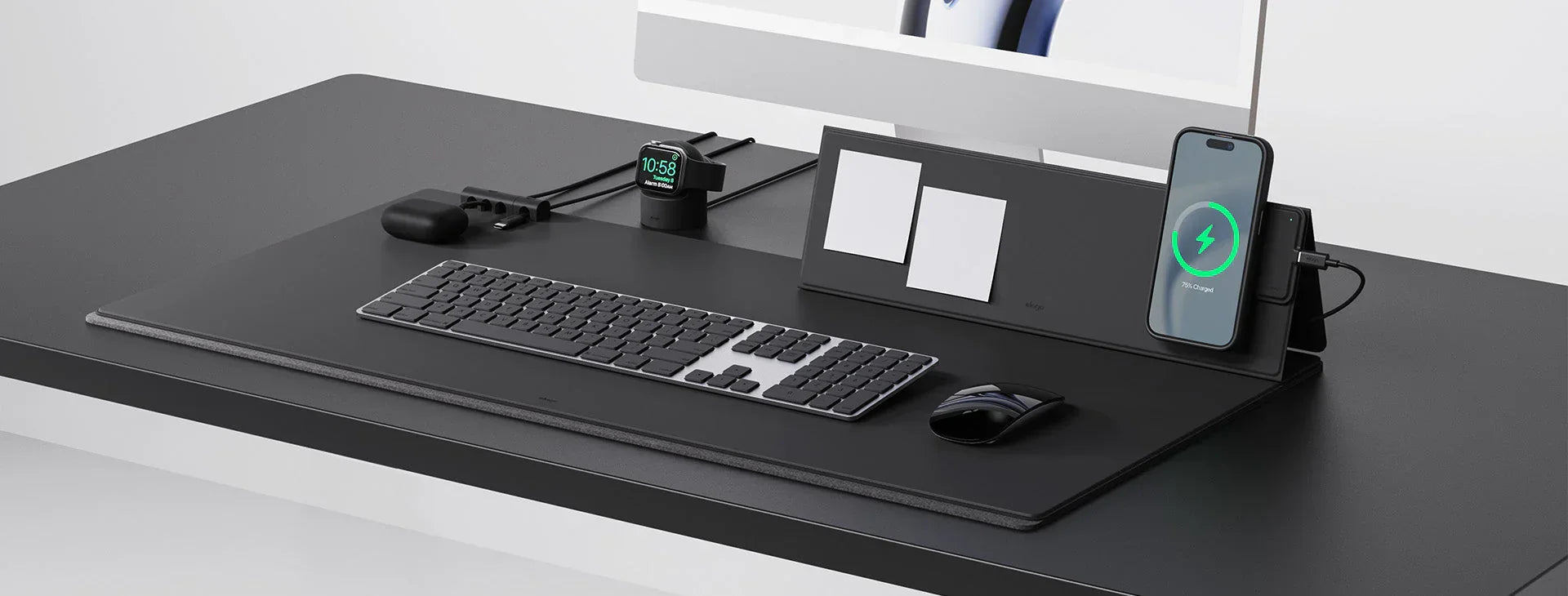 Modern tech workspace with wireless keyboard, mouse, charging phone, smartwatch, and desk organizer
